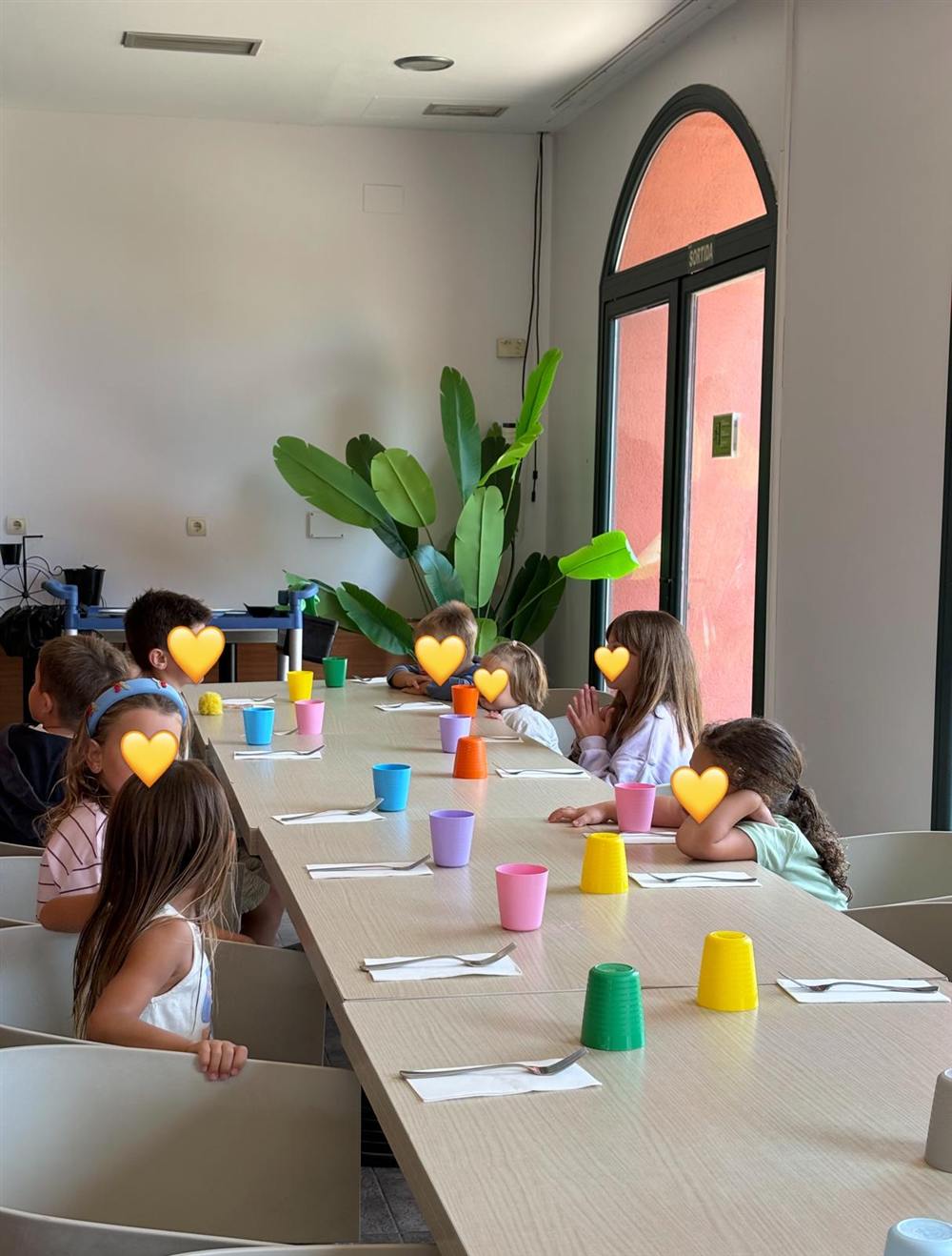 Niños comiendo en una mesa larga con vasos de colores